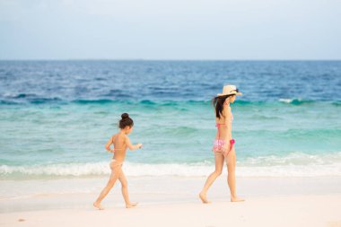 Anne ve kızı kumlu sahilde dinleniyor.