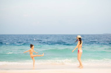 Anne ve kızı kumlu sahilde dinleniyor.