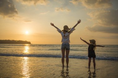 Anne ve kızı gün batımında kumsalda oynuyorlar.
