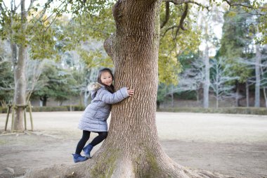 Küçük kız parkta bir ağacın yanında oynuyor.