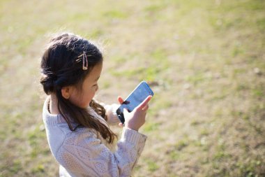 Parkta akıllı telefonla oynayan genç bir kız.