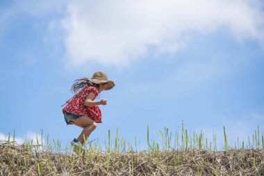 Hasır şapkayla tarlada zıplayan tatlı Asyalı küçük kız.