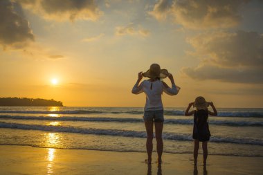 Anne ve kızı gün batımında kumsalda oynuyorlar.