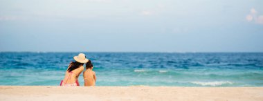 Anne ve kızı kumlu sahilde dinleniyor.