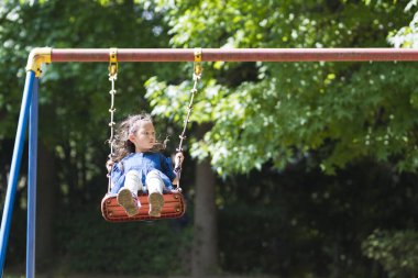 Küçük kız yaz parkında sallanıyor..