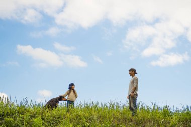 Baba, kız ve köpek çayırda oynuyorlar.
