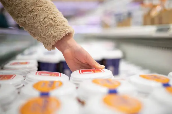 The hand of a child picking up yogurt at a supermarket