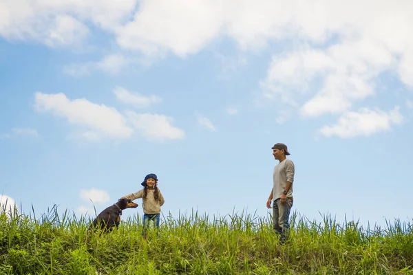 Baba, kız ve köpek çayırda oynuyorlar.