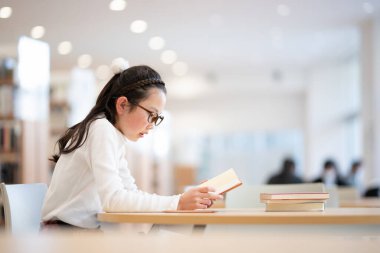 Kütüphanede kitap okuyan genç bir kız öğrenci. 