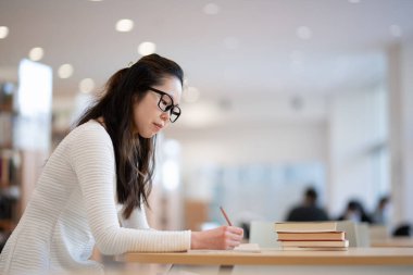 Genç bayan öğrenci kütüphanede okuyor. 