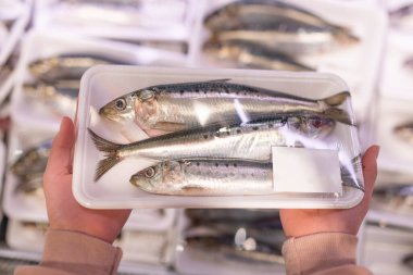 Piyasada plastik bir kabın içinde balıklı eller