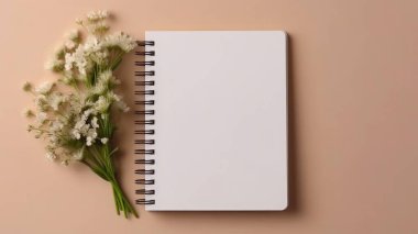 Masadaki beyaz boş defter ve çiçeklerin üst görünümü