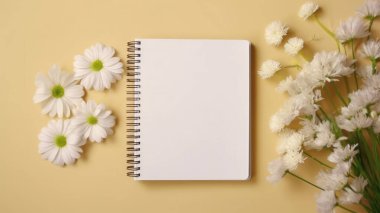 Masadaki beyaz boş defter ve çiçeklerin üst görünümü