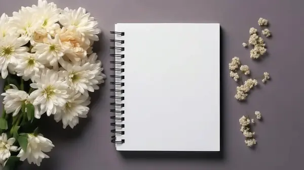 Masadaki beyaz boş defter ve çiçeklerin üst görünümü
