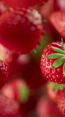 Çilek grubunun animasyonu. Birçok çilek uzayda arka planda yavaşça döner. Dikey kompozisyon. Defoktus. Yakın plan..