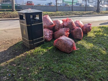 A Red Bin Bags Piling Up on A Street Corner Waiting to Be Collected Next To A Metal Bin