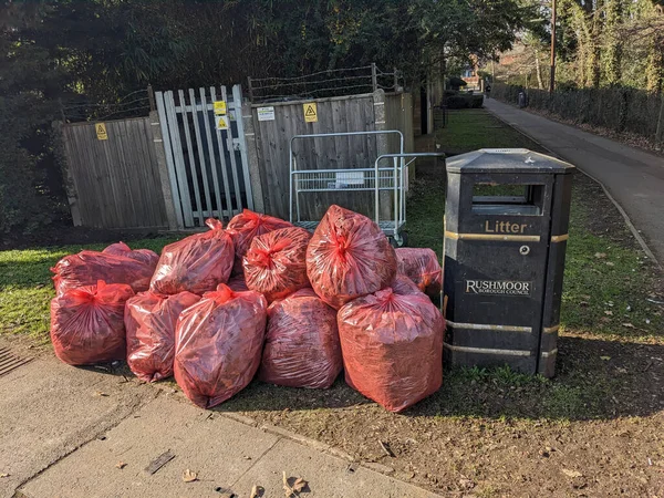 A Red Bin Bags Piling Up on A Street Corner Waiting to Be Collected Next To A Metal Bin