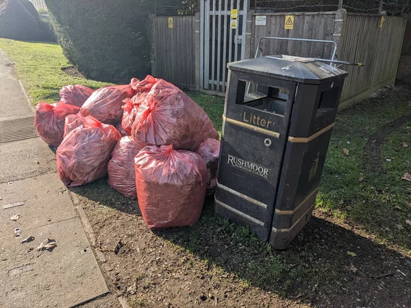 A Red Bin Bags Piling Up on A Street Corner Waiting to Be Collected Next To A Metal Bin