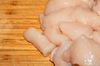 Ahşap kesim tahtasının üzerinde doğranmış çiğ tavuk etini yakın.