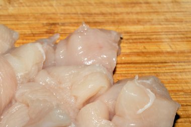 Ahşap kesim tahtasının üzerinde doğranmış çiğ tavuk etini yakın.