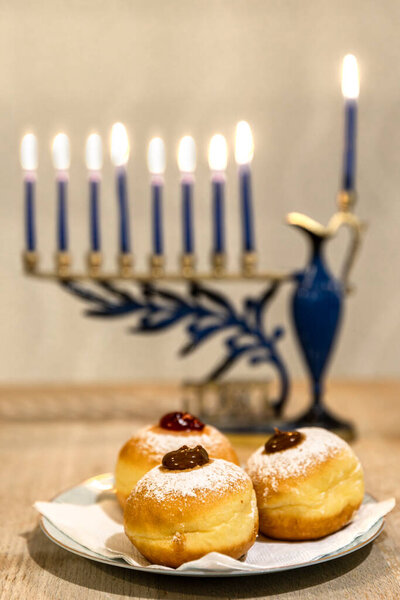 Красивая Менора, Ханукая с 8 зажженными свечами для еврейского праздника Ханука на столе. Празднование праздника огней Хануки. Суфганийот пончики сладкие культурные блюда на тарелке в фокусе