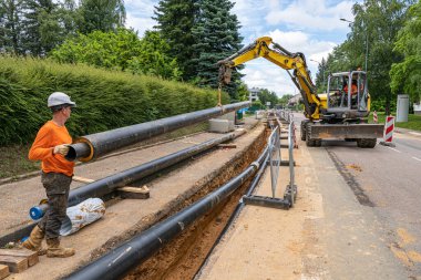 Process of laying of heating system pipelines in a city street. Extension of a heating network. Heat water pipes in a trench. Buried underground network. Normandy, France, June 2021 clipart