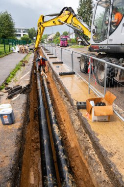 Process of laying of heating system pipelines in a city street. Extension of a heating network. Heat water pipes in a trench. Buried underground network. Normandy, France, June 2021 clipart
