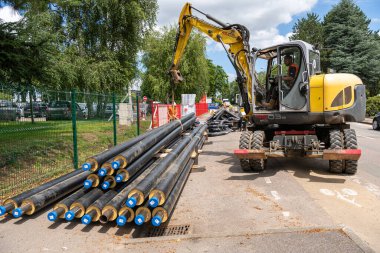 Process of laying of engineering of heating system pipelines in a city street. Heat water pipes in a trench. Storage of pipes on the roadway before work. Normandy, France, June 2021 clipart