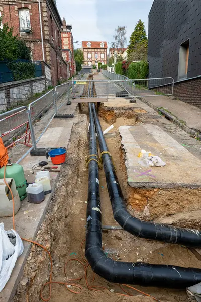 Process of laying of heating system pipelines in a city street. Extension of a heating network. Heat water pipes in a trench. Buried underground network. Normandy, France, October 2022