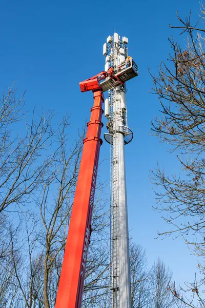 Deployment of the 5G network. Installation of antennas on a mobile telephony mast using a bucket truck. Poplar trees in the foreground. France, Normandy, December 2022