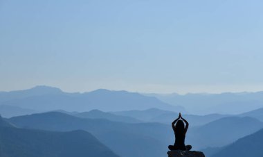 Güzel bir manzarada yoga yapan genç bir kadının silueti.