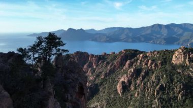 Fransa 'nın Korsika kentindeki Calanques de Piana' ya tepeden bakan sakin bir gölün yanındaki dağın tepesinde bir adam duruyor..