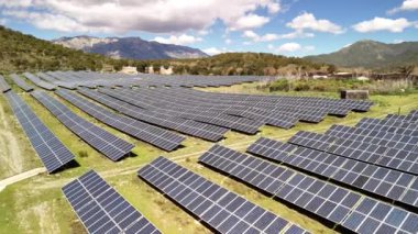 Yeşil enerji üreten geniş bir güneş paneli alanı, yüksek dağların arka planına kurulur..