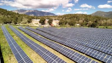 Korsika 'da yeşil enerji üreten, arka planda dağlar olan bir alanda sıralanmış güneş panelleri..
