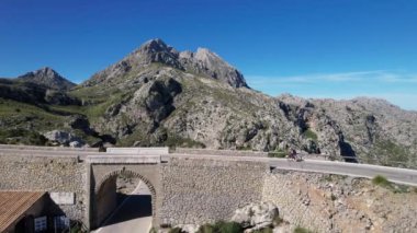 Bir bisikletçi dağlarda taş bir köprüye biner. Palma de Mallorca 'daki görkemli dağların zemininde taş bir köprü duruyor. Kısa kod: 776143084