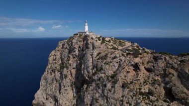 Gün batımında kayalık bir uçurumun tepesine tünemiş ikonik Cape Formentor deniz fenerinin nefes kesen hava görüntüsü..