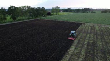 Bir traktör bulutlu bir öğleden sonra Danimarka kırsalında tarla sürüyor..