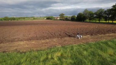 Genç bir kız, yeni sürülmüş bir tarlanın yakınındaki toprak yolda bisiklet sürüyor..