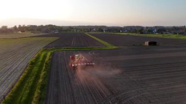 Gün batımında bir tarlaya mineral gübre uygulayan bir traktörün hava görüntüsü..