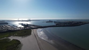 Zeebrugge kargo limanının geniş bir görüntüsü büyük bir gemi kenetlenmiş ve arka planda vinçler, ön planda kumlu bir plaj..
