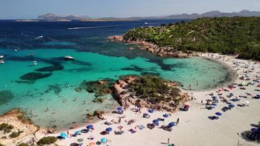 Sardunya 'daki el değmemiş bir plajın panoramik görüntüsü, berrak turkuaz sular, beyaz kumlar ve güneş ve denizin keyfini çıkaran insanlar..