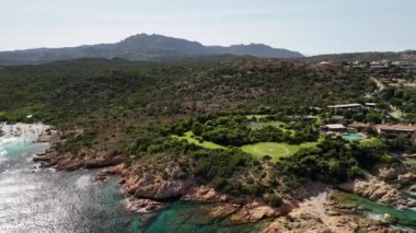 İtalya 'nın Sardunya kıyısındaki yemyeşil ve dramatik uçurumların arasına yerleşmiş lüks bir tatil beldesinin panoramik bir görüntüsü..