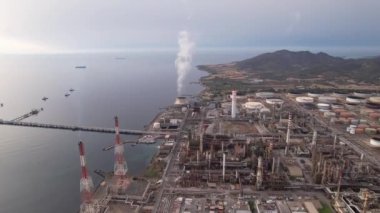 Sardunya 'da sanayi bölgesinde çalışan bir termik santral bacasından yükselen duman ve yakındaki limanda görülebilen gemilerle çalışıyor..