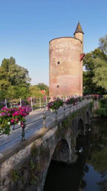 Çiçek sepetleriyle kaplı büyüleyici bir köprü Belçika 'nın güzel Bruges şehrinde tarihi bir taş kuleye doğru yol alıyor..