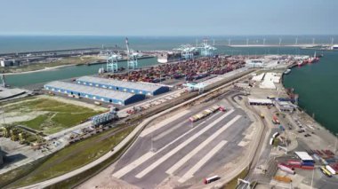 Belçika 'daki Zeebrugge lojistik merkezindeki yoğun bir konteynır terminalinin hava görüntüsü. Gemiler, kamyonlar ve vinçler malları limana getirip götürüyor..