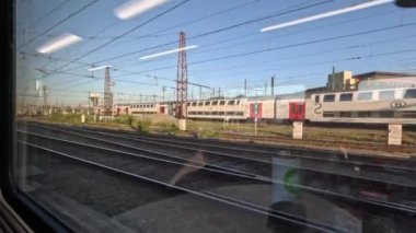 Tren, başka bir trenin penceresinden görülen bir raydan geçiyor. Hava açık ve güneşli..