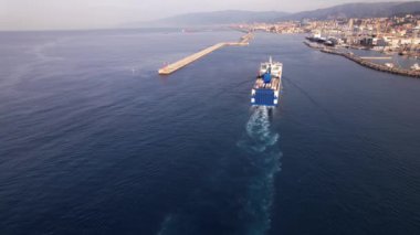 Genova limanına yaklaşan bir kargo gemisi, güneş kıyı şehri üzerinde parıldarken, hareketli limana konteynırlar getiriyor..