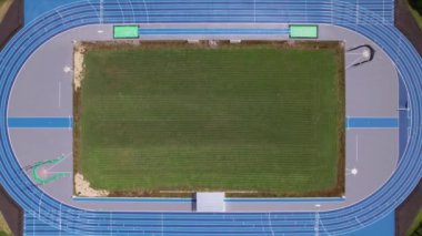 Hava manzarası, açık gökyüzünün altında koşu pisti ve saha alanı bulunan atletizm stadyumunun düzenini gösteriyor..