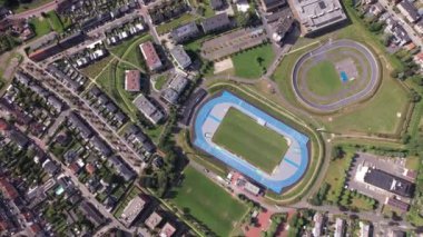 Konut binaları ve yeşil alanlarla dolu kentsel bir mahallenin ortasındaki canlı bir atletizm stadyumunun planını araştırın..