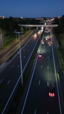 Arabalar karanlık çöktüğünde yoğun bir otobanda yol alır. Arka planda şeritleri aydınlatan farlar ve şehrin ışıkları vardır..